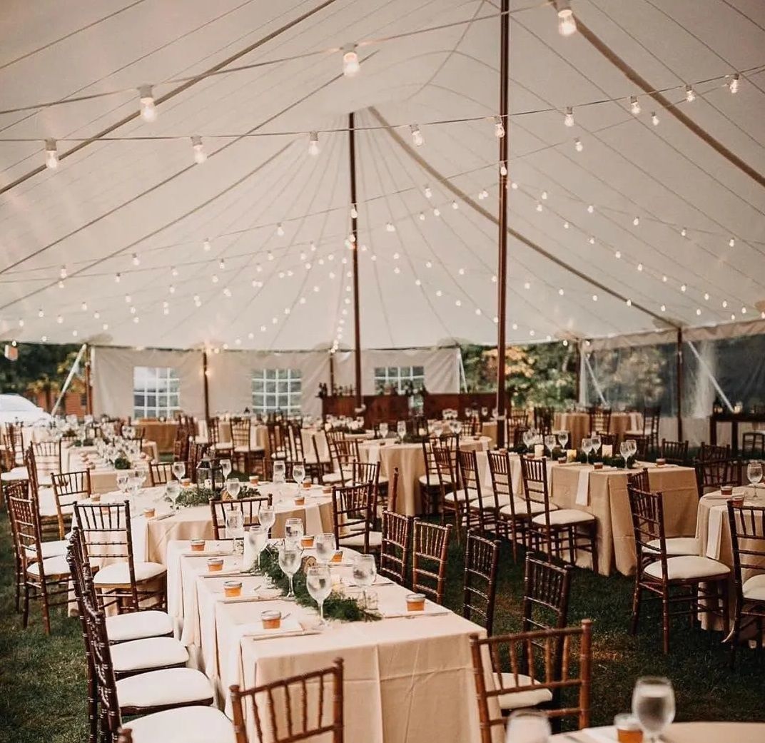 Elegant tented event venue with string lights and long dining tables set for a reception