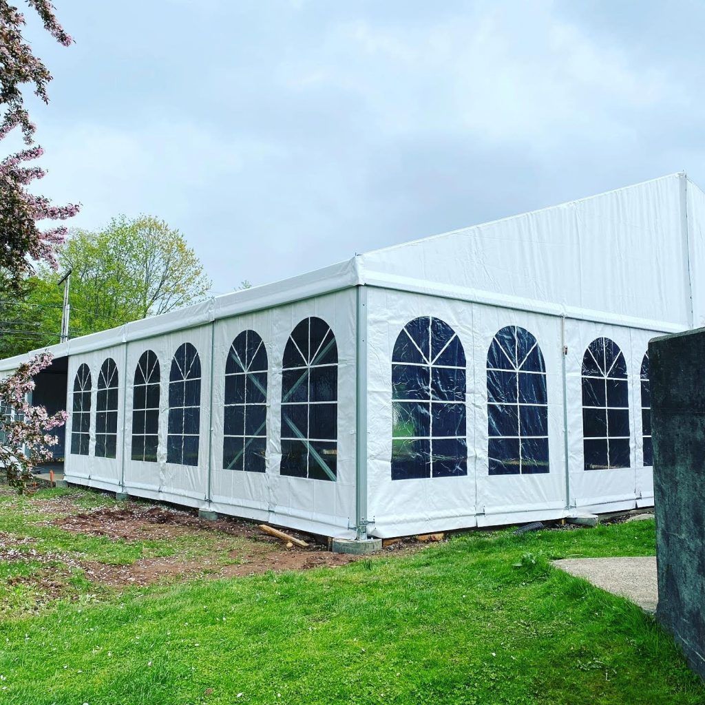 White tent with arched windows set on green grass under a cloudy sky.