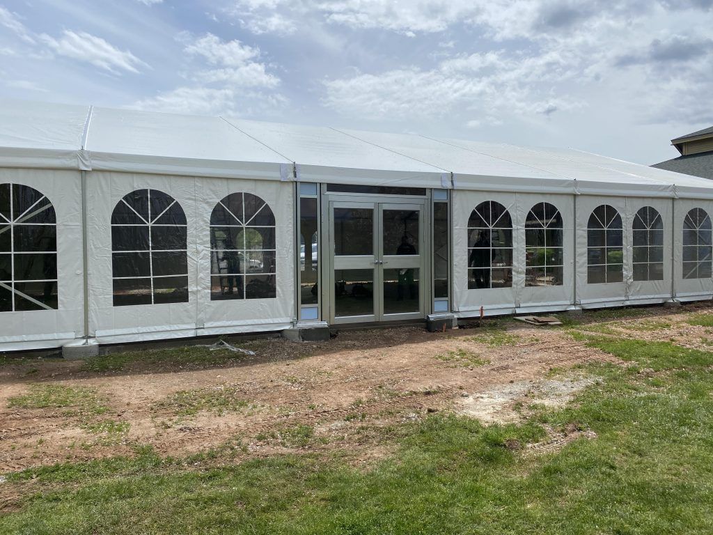 White tent with arched windows and a glass door, set on grass under a cloudy sky.