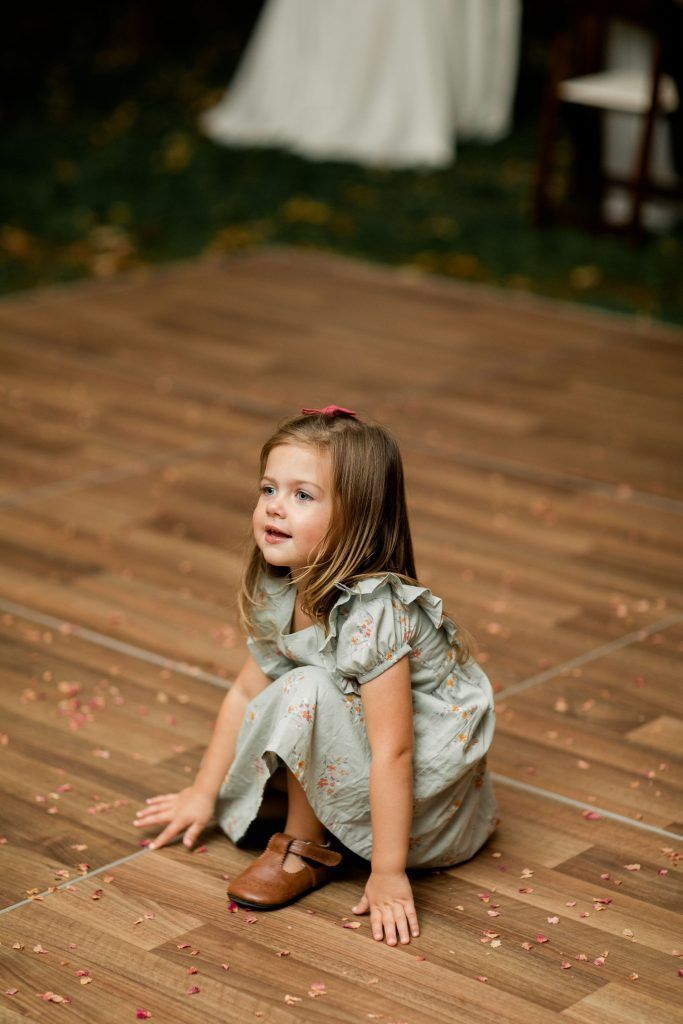 Young girl in blue dress on a wooden dance floor, looking up, hands on floor.