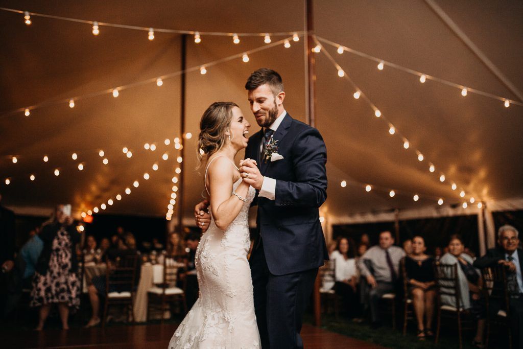 Bride and groom dance under string lights in a tent at wedding reception.