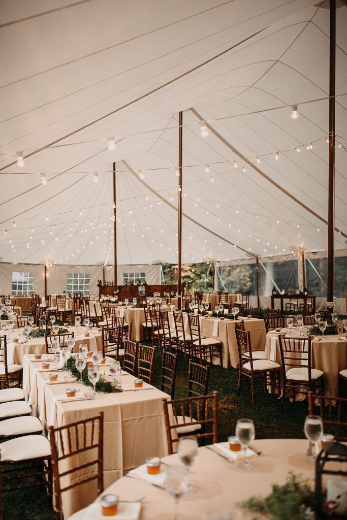 Wedding reception tent with tables, chairs, and string lights.