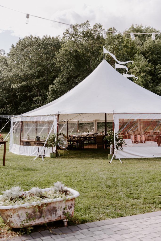 White tent set up on a grassy lawn for an event with a vintage bathtub planter in the foreground.