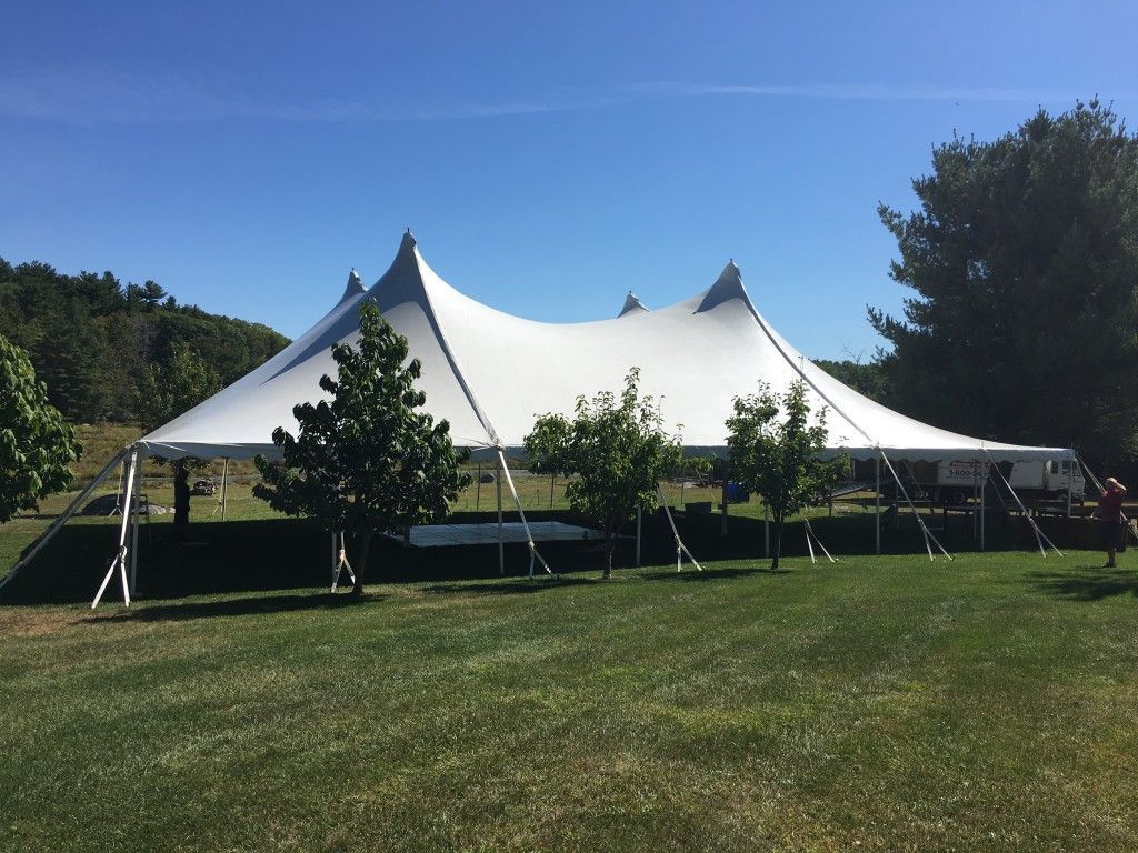 White tent with multiple peaks set up on a grassy field on a sunny day.