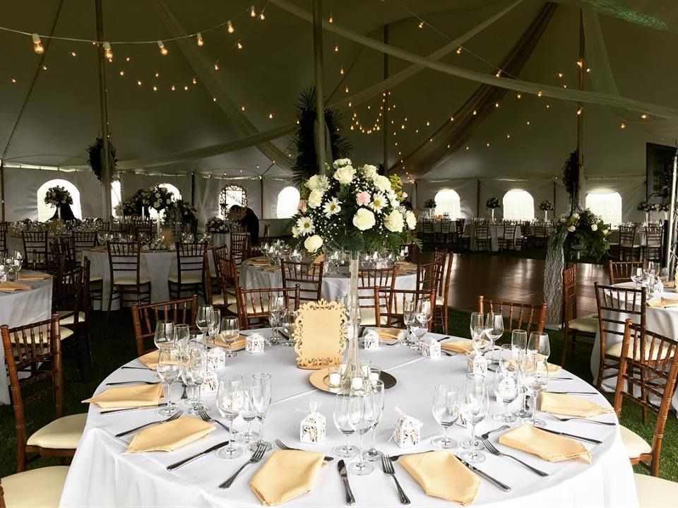 Wedding reception in a white tent with round tables set with white linens, flowers, and place settings.