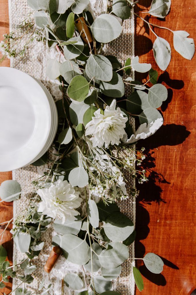 Table setting with white plates and floral garland on a rustic wooden surface.