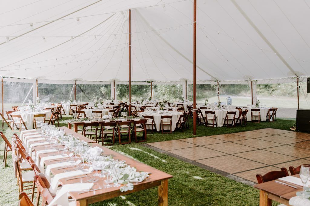 Wedding reception tent with tables, chairs, and a dance floor on a grassy lawn.