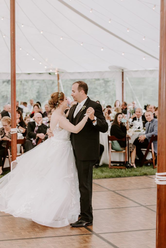 Bride in white dress dances with a man in a black suit on a wooden dance floor in a tent.