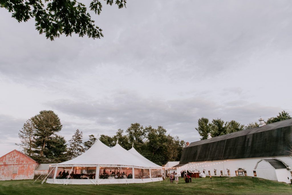 White tent and barn at outdoor wedding reception under cloudy sky.