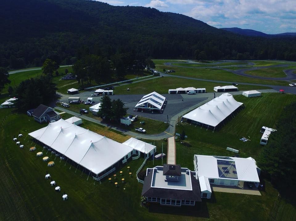 Aerial view of white tents on a grassy field, mountains in the background.