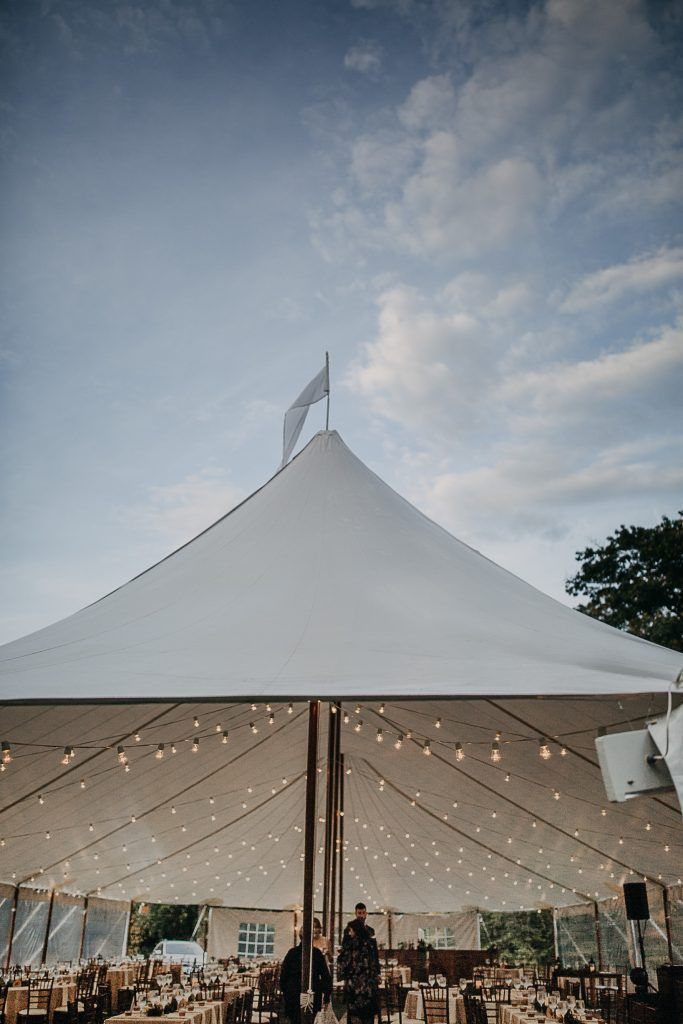 White tent with string lights, set for an event under a cloudy sky.