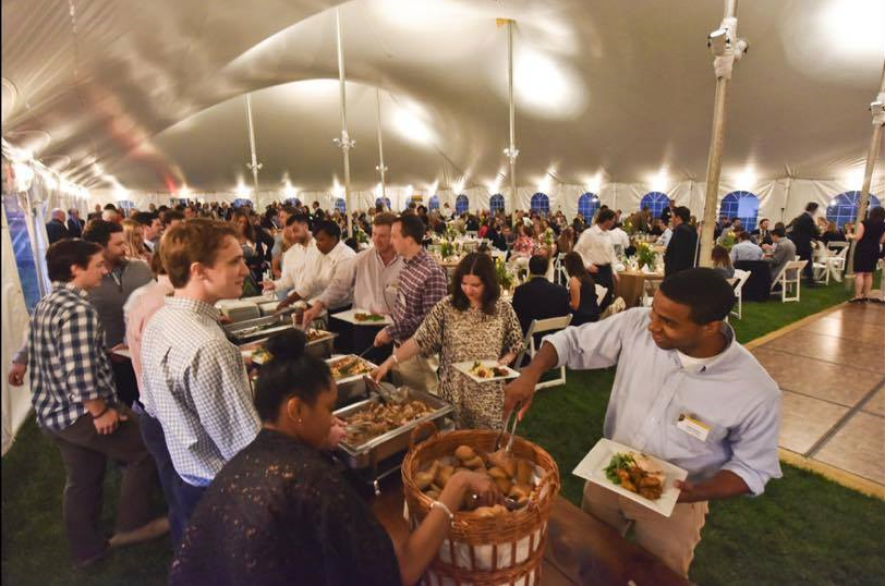 People serving themselves at a buffet inside a large tent.