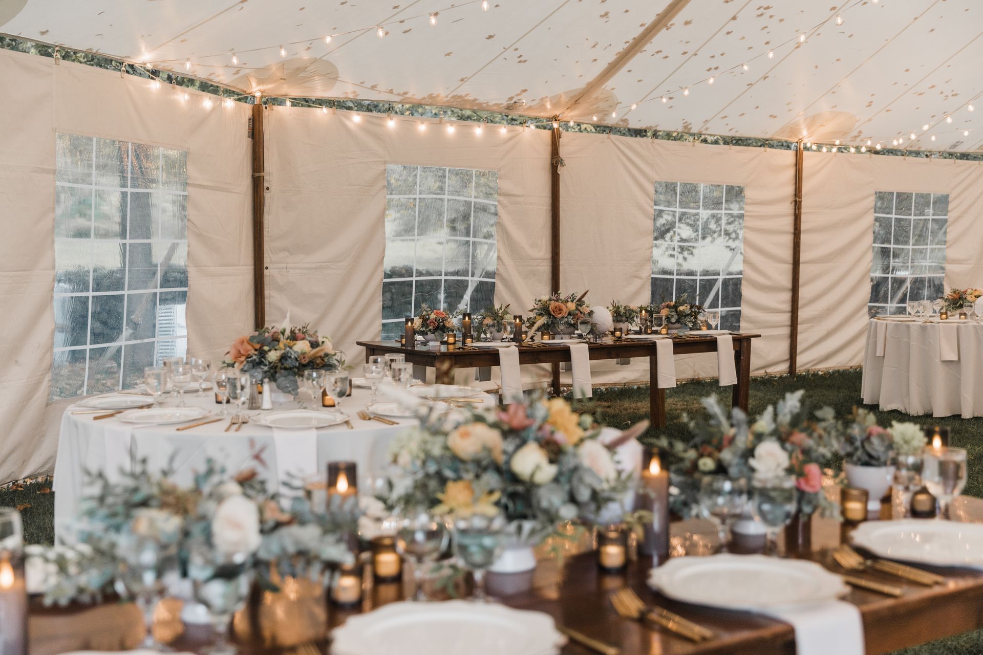 Wedding reception tent with tables, floral centerpieces, and string lights.