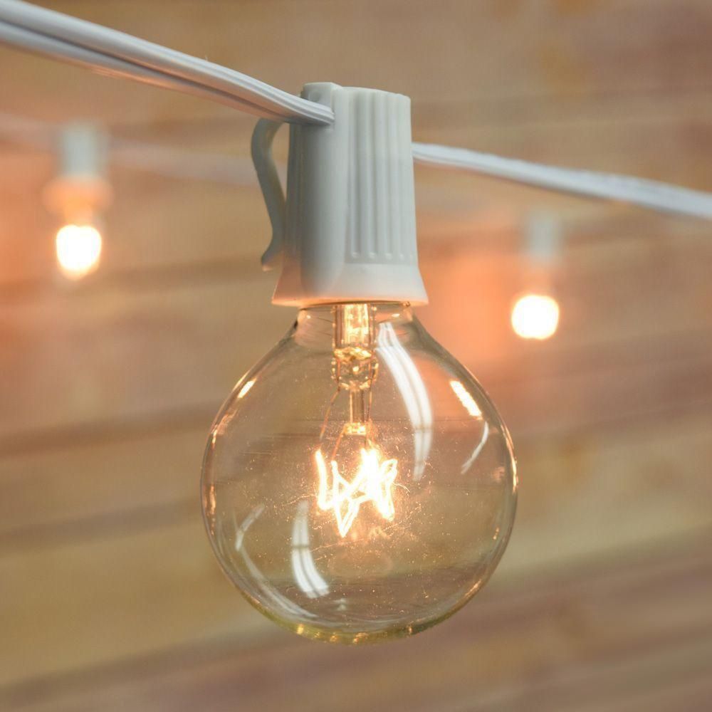 Close-up of a lit, round light bulb in a white socket attached to a white wire; wooden background.