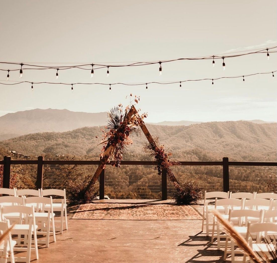 Wedding ceremony setup on a mountain with wooden arch decorated with flowers, string lights, and white chairs.