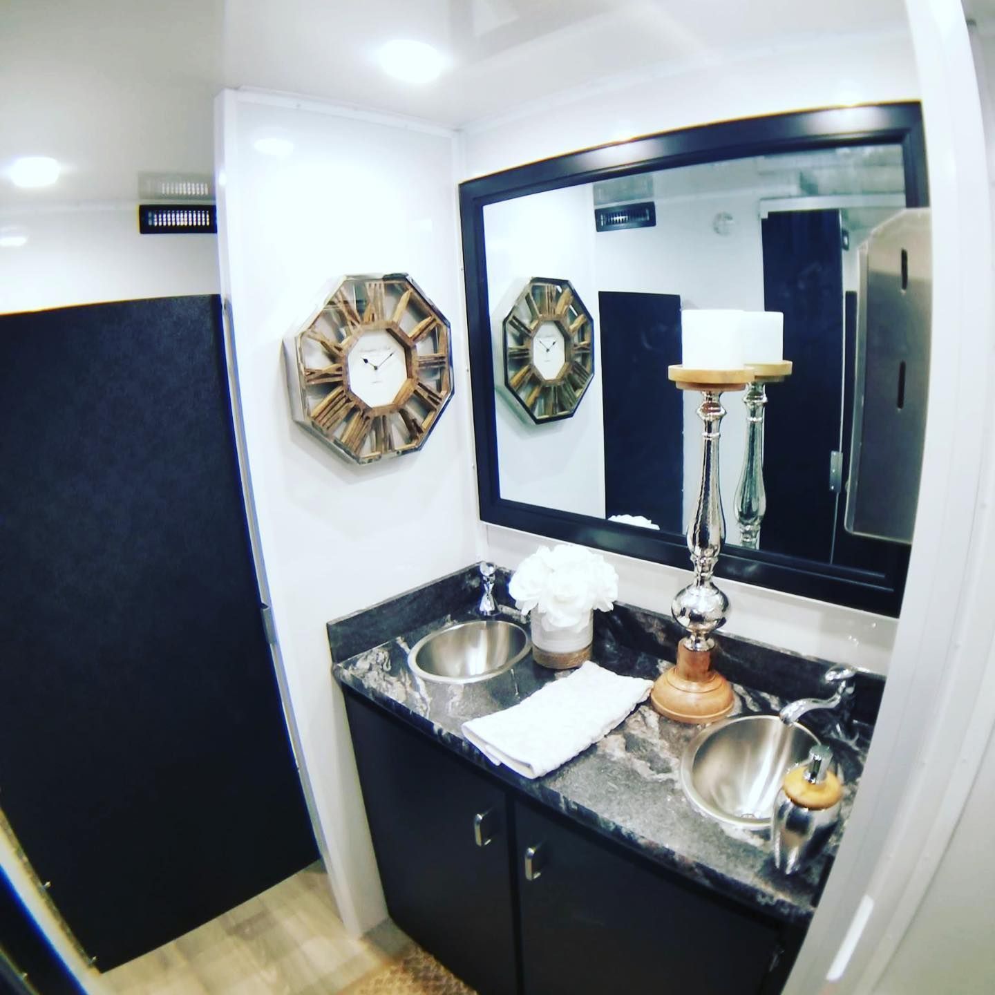 Interior of a luxury portable restroom with black and white decor; two sinks, large mirror, and decorative candle holders.