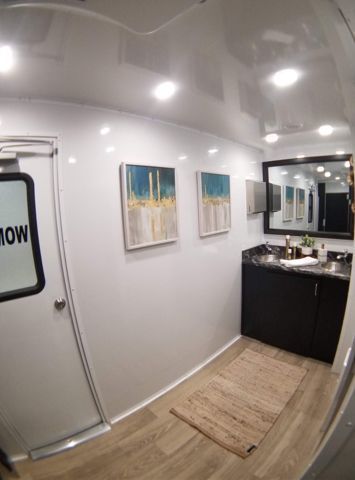 Interior of a portable restroom with white walls, paintings, a black vanity, and a mirror.