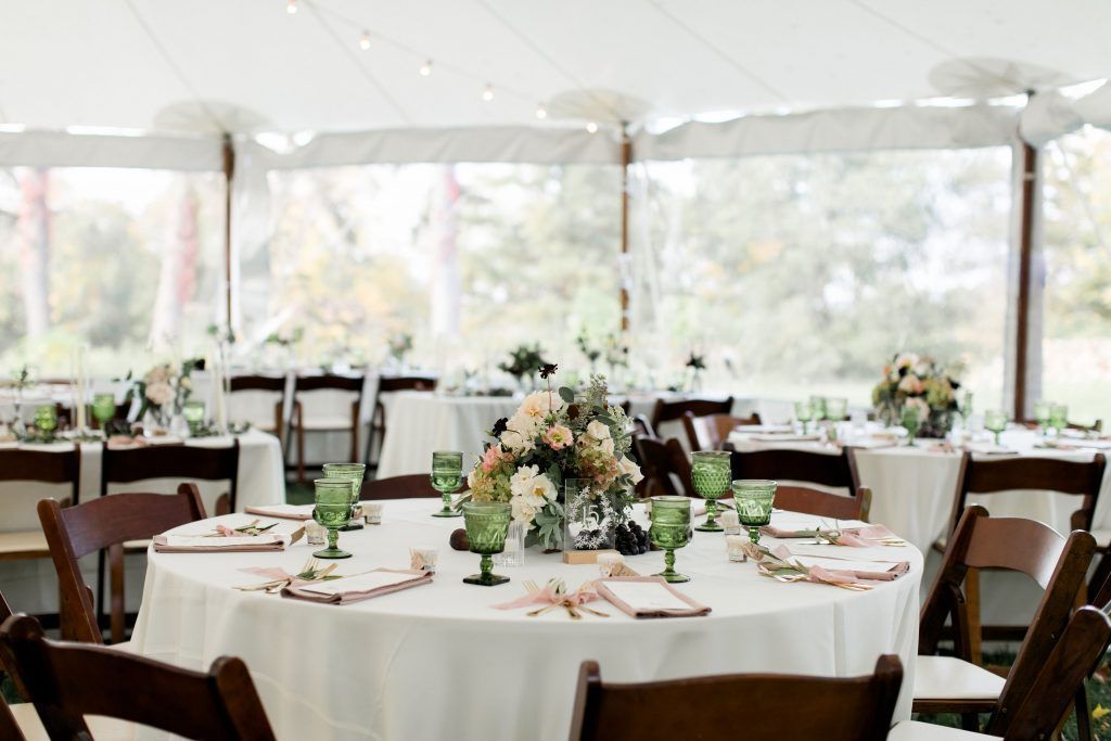 Wedding reception tent with round tables set with flowers and green glasses.