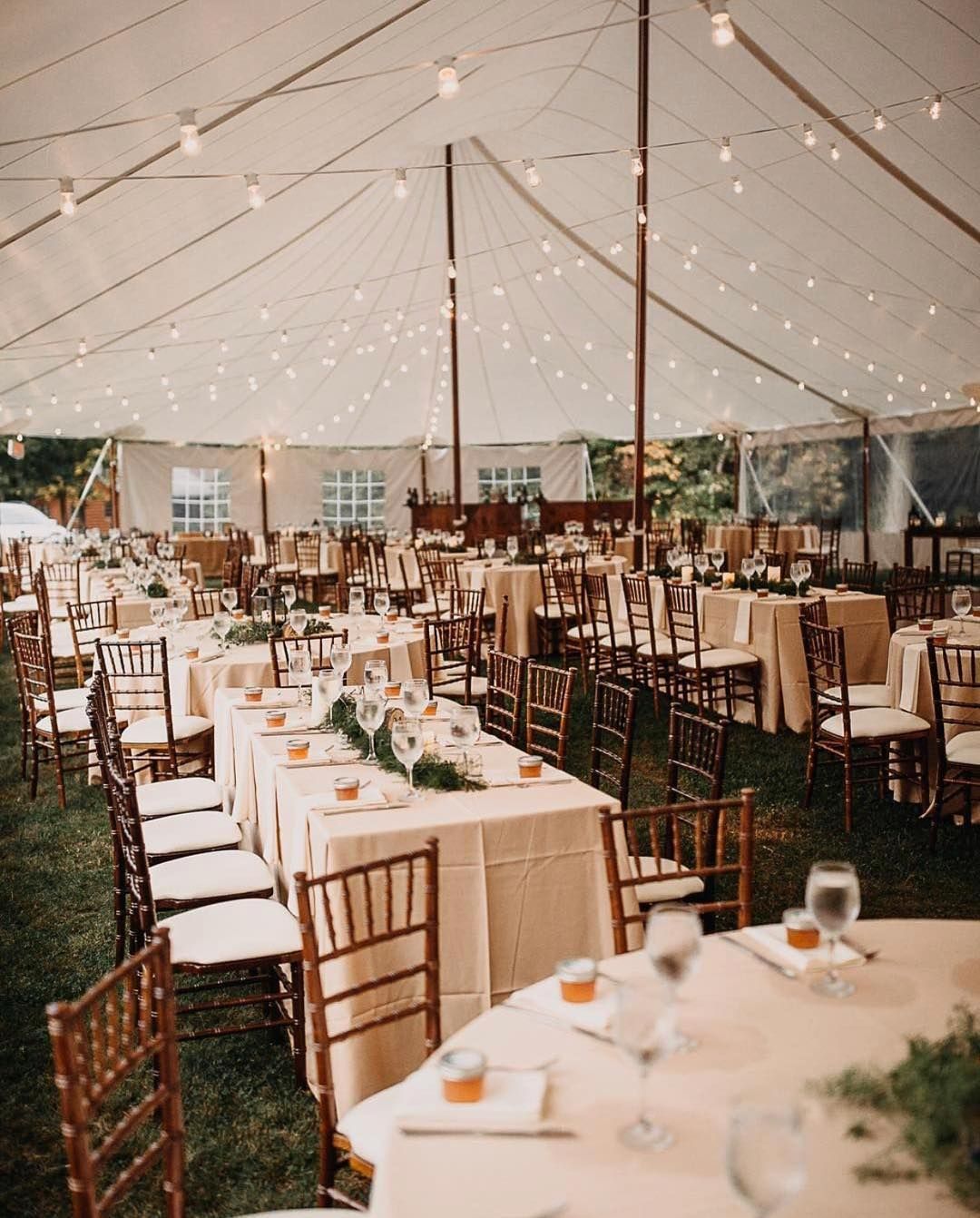 Wedding reception inside a tent, tables set with beige linens, string lights overhead.