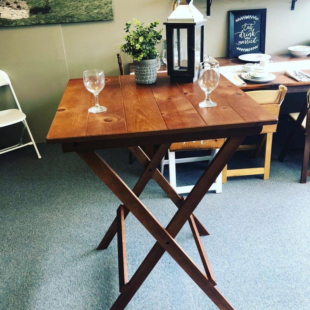 Wooden folding table with two wine glasses, a plant, and a lantern on top.