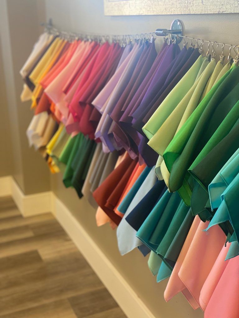 Colorful fabric swatches hanging on a silver rack, arranged in rainbow order along a white wall.