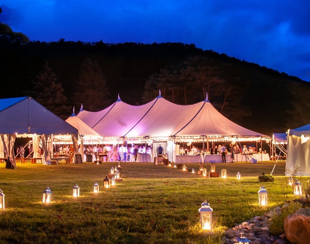 Lit tents at a nighttime outdoor event; lawn, lanterns, and distant figures.