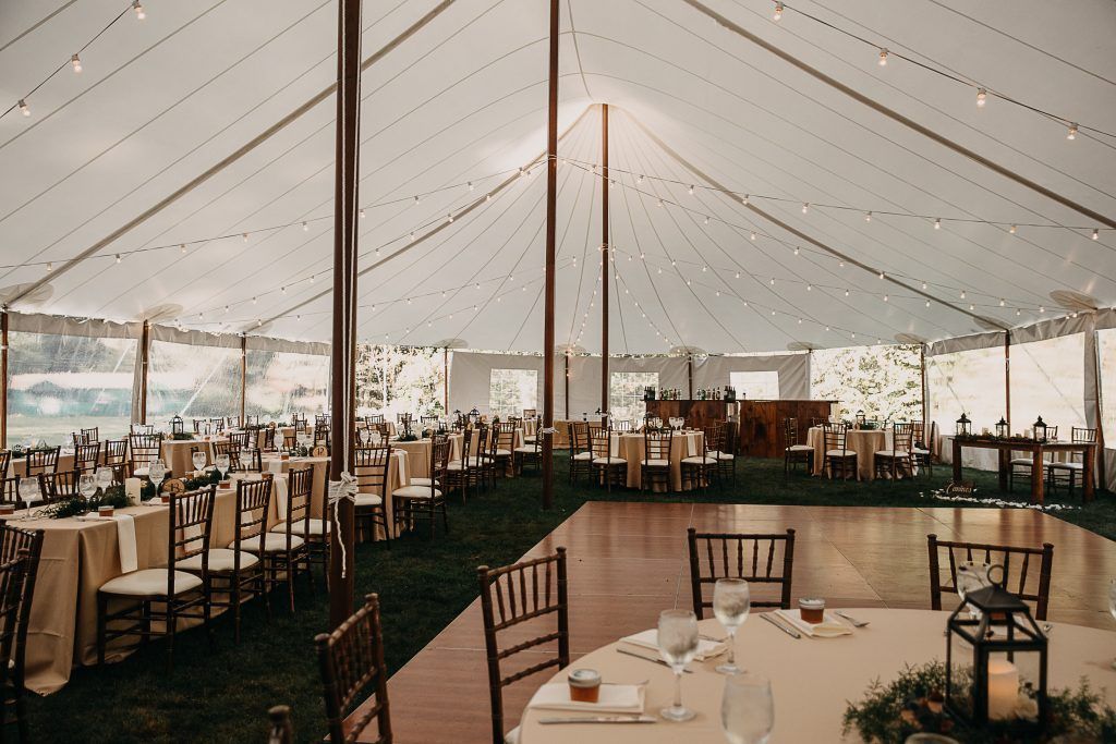 Wedding reception tent with tables, chairs, dance floor, and string lights.