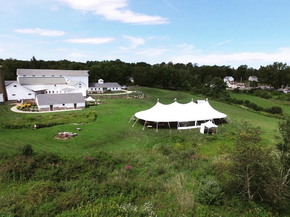 White tent on a grassy hill with buildings and trees in the background under a blue sky.