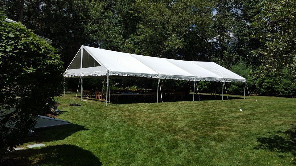 White event tent on a grassy lawn surrounded by trees on a sunny day.
