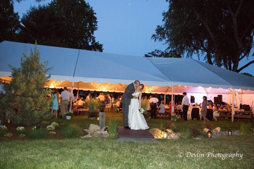 Couple kissing under a large tent at a wedding reception at dusk.