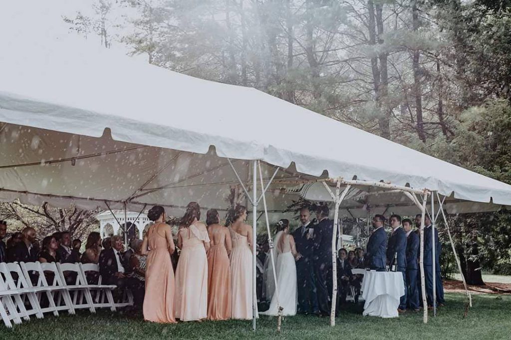 Wedding ceremony under a white tent; bridesmaids in pastel gowns stand near the altar.
