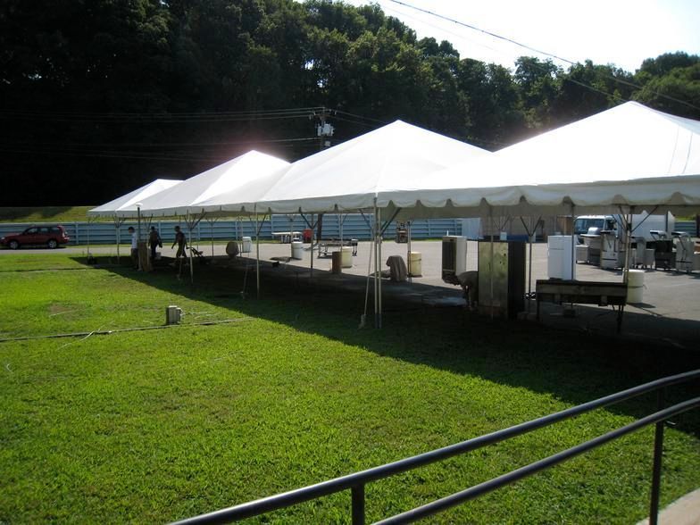 White tents set up on a grassy area; people working at tables inside.