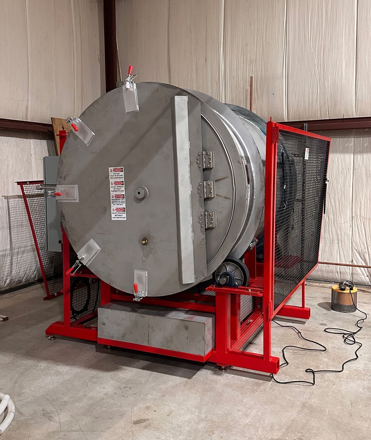 Large, silver industrial drum on a red frame, with safety fencing. Indoors.