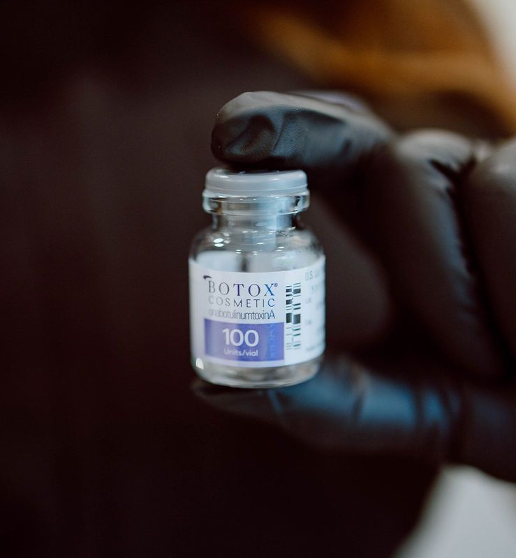 Small vial of Botox cosmetic held by a gloved hand. The vial has a white label with blue text reading 