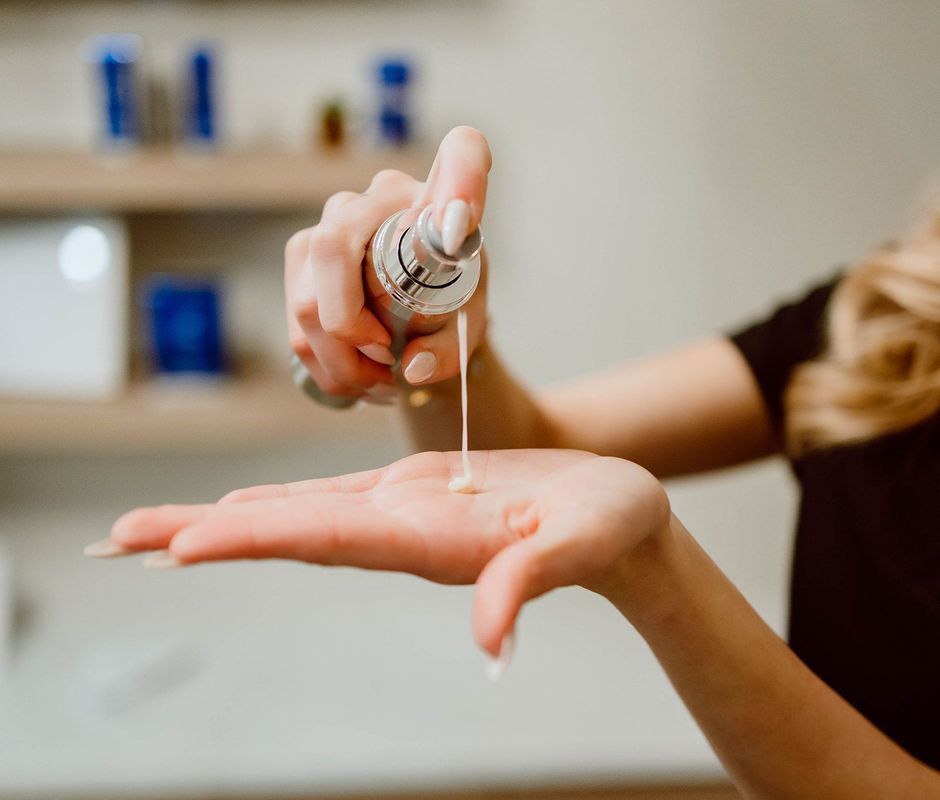Person dispenses lotion from a bottle into their hand. Creamy liquid falls into an open palm. Indoor setting.