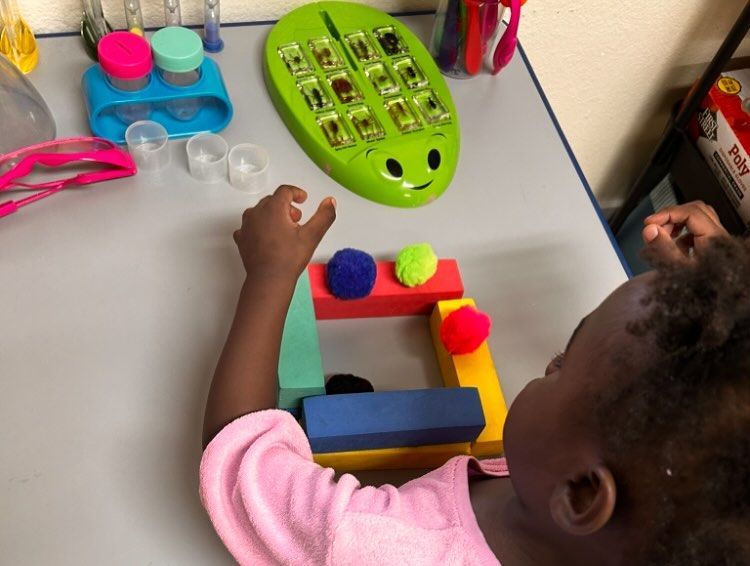 Child playing with colorful blocks and pom-poms near a ladybug-shaped game on a table.