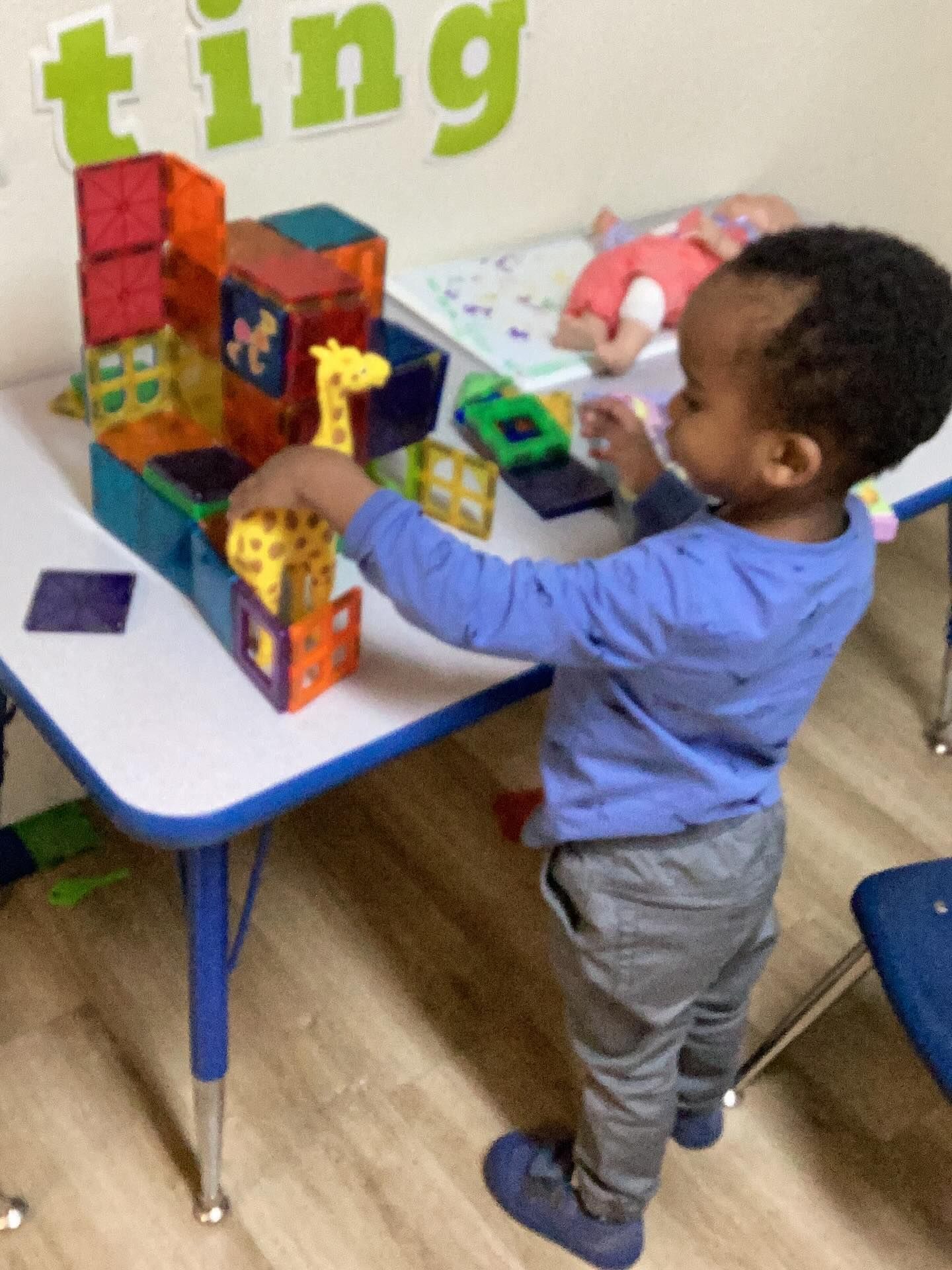 Child playing with magnetic blocks and a giraffe toy at a table.