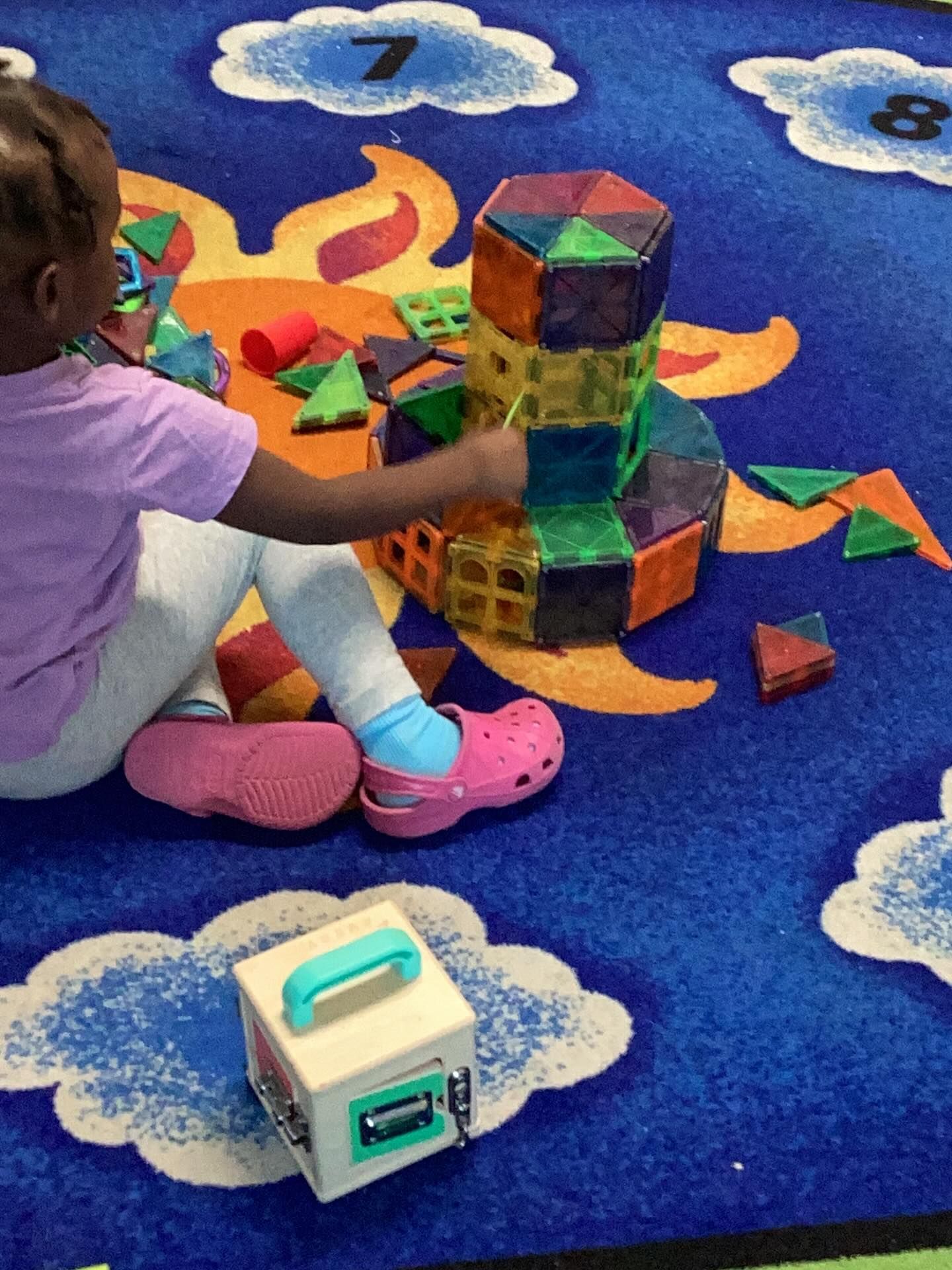Child playing with magnetic building tiles on a blue patterned rug with a toy.