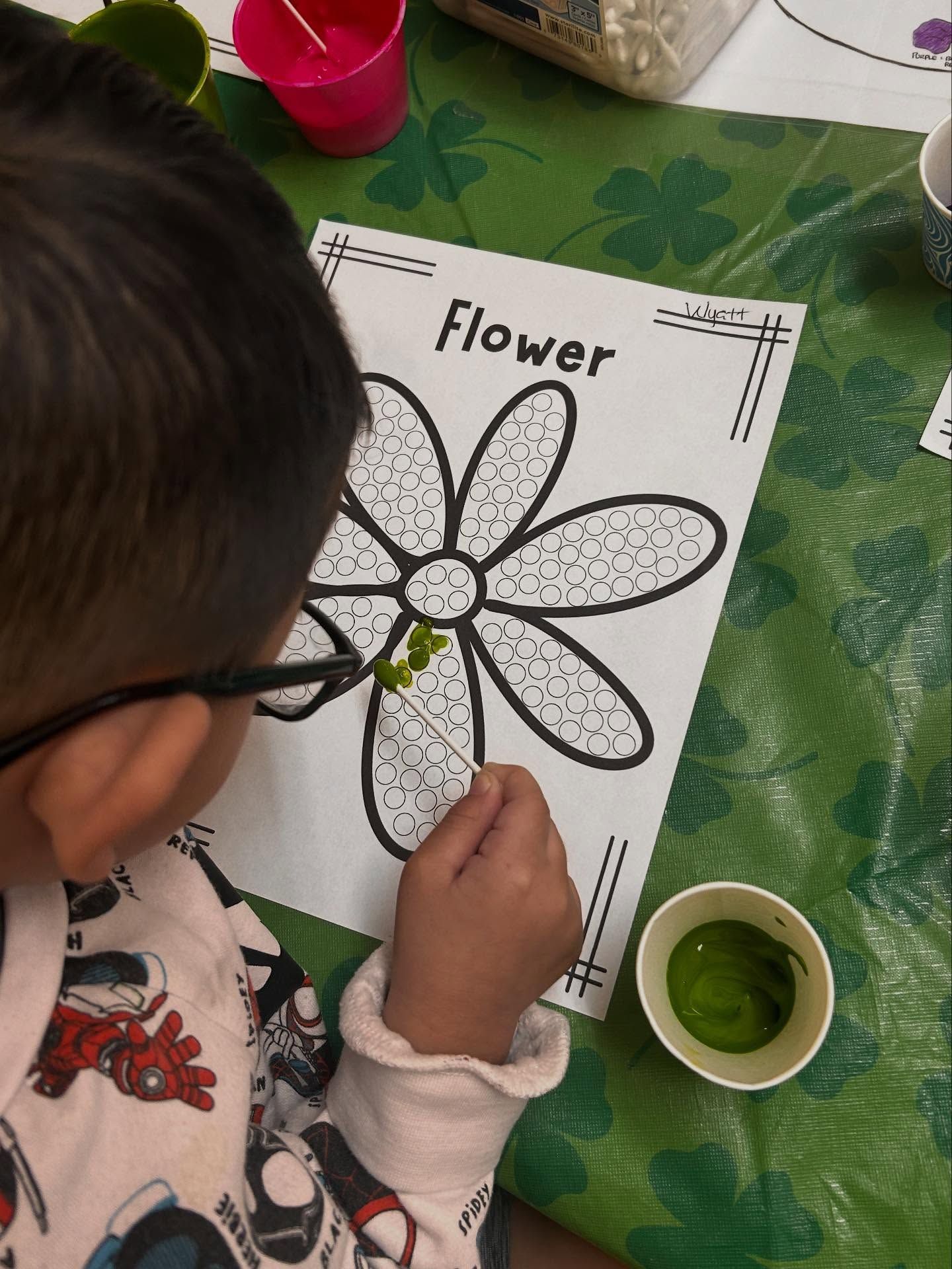 Child painting a flower template with green paint at a table.