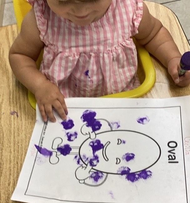 Child at table, coloring oval drawing with purple marker.
