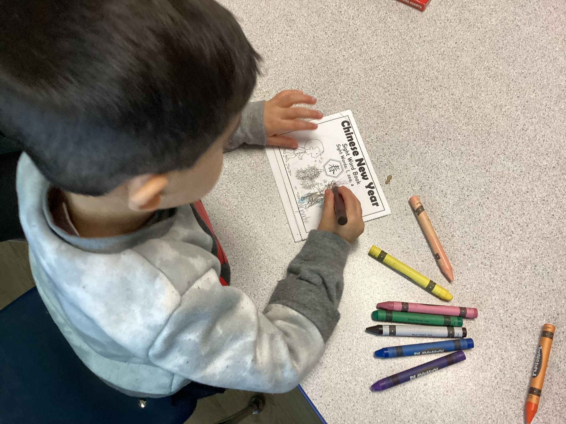 Young child coloring a worksheet with crayons while sitting on the foor.
