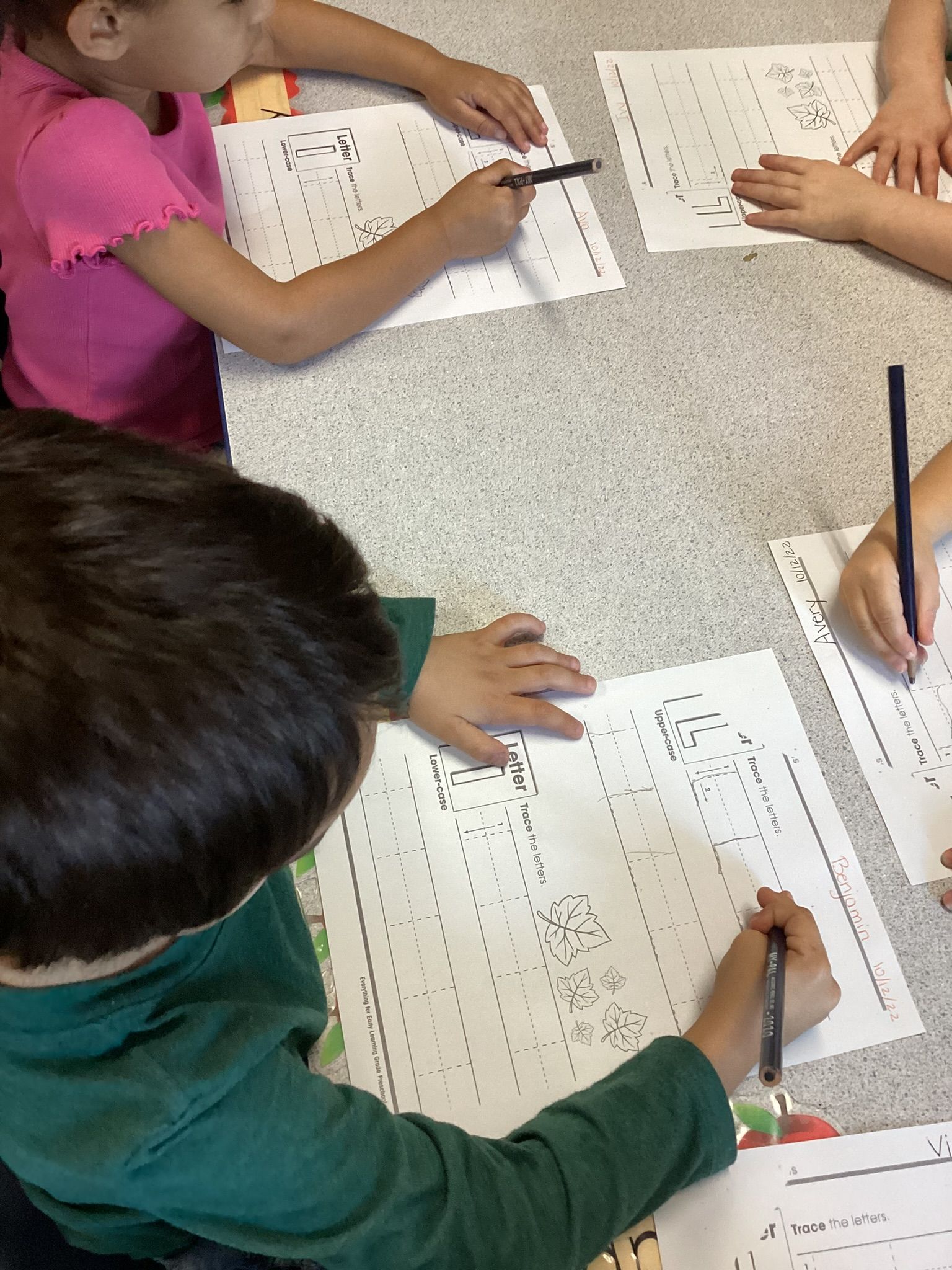 Two children working on learning worksheets together at a classroom table.
