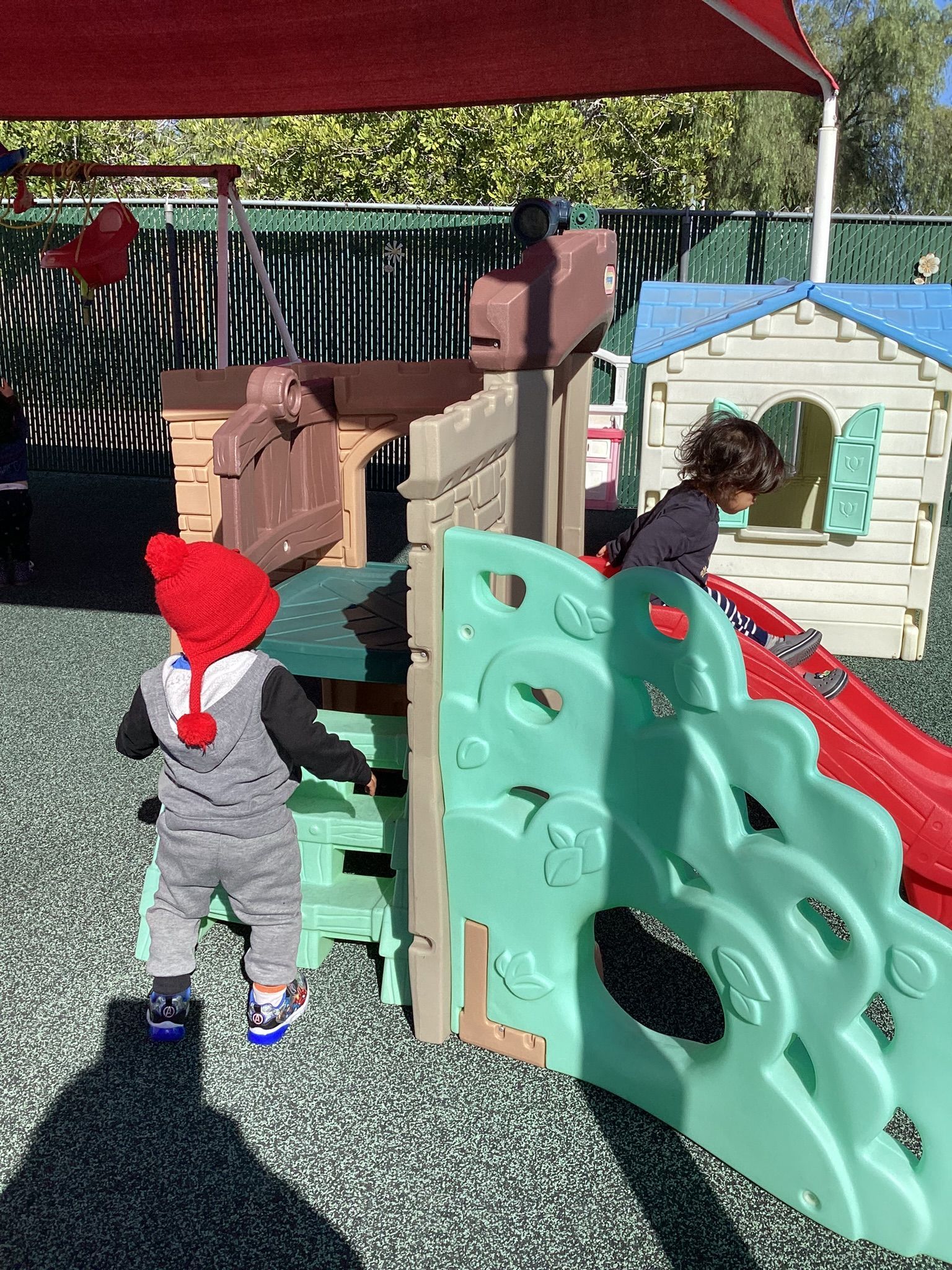 Children playing on outdoor playground with slide and climbing structure.