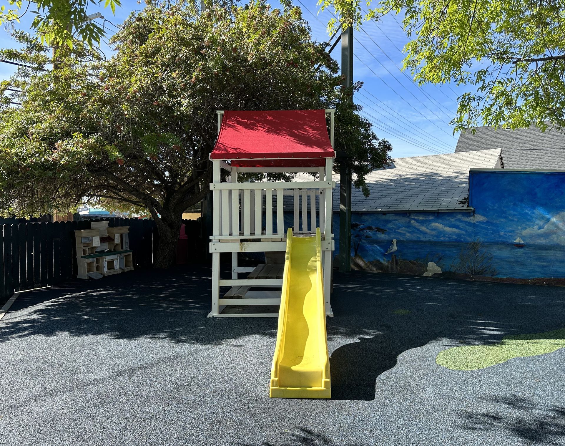 Play structure with a yellow slide and red roof in a playground.