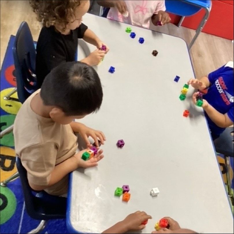 Children sitting at a table playing with colorful blocks. Classroom setting.