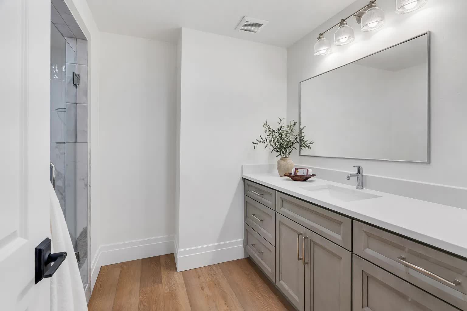 Bathroom with gray vanity, white countertop, large mirror, and wood flooring.