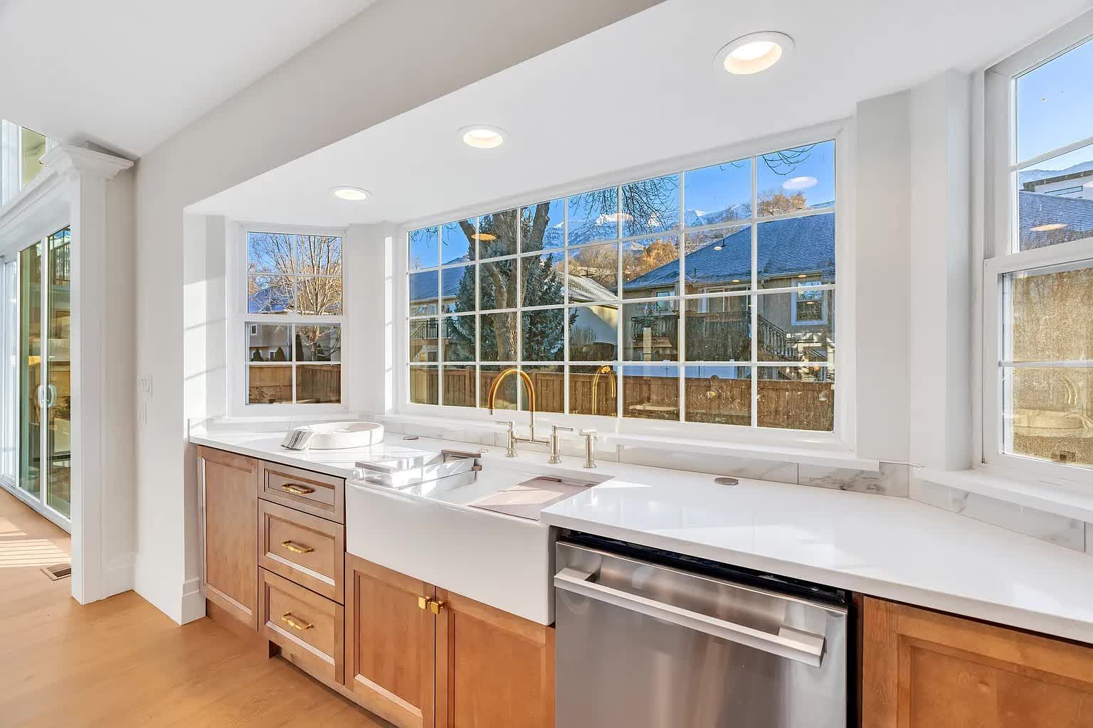 Kitchen with a large bay window, light wood cabinets, white countertop, and a stainless steel dishwasher.