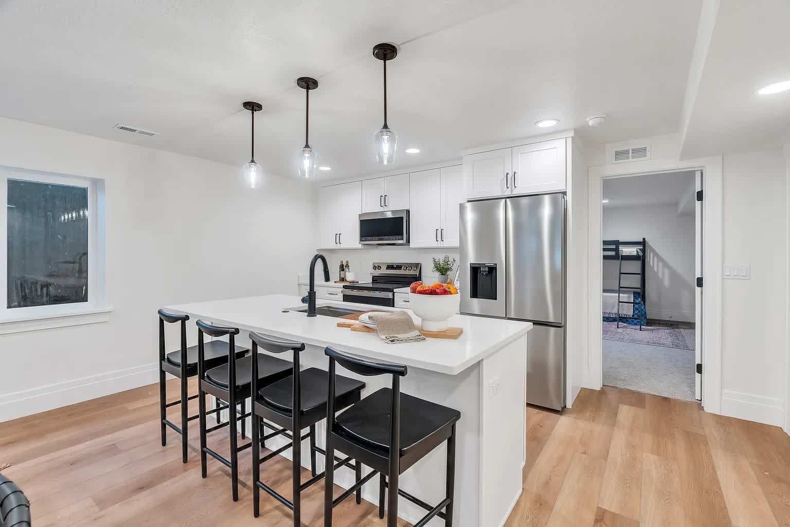 Modern kitchen with island, pendant lights, stainless steel appliances, and wood flooring.
