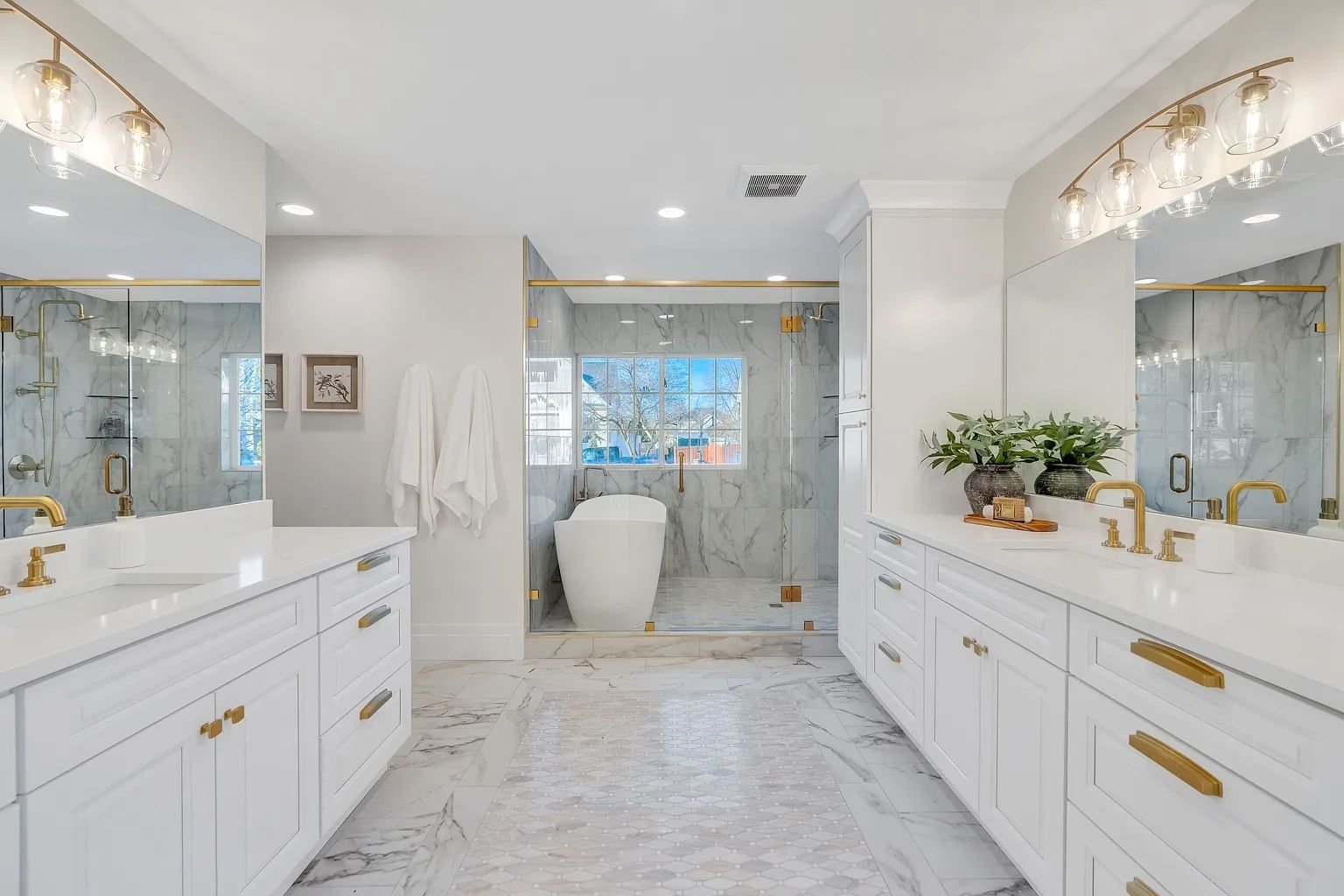Spacious white bathroom with marble floors, double vanity, and glass shower. Gold accents and decorative lighting.