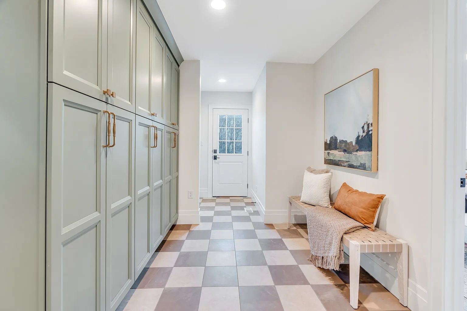 Hallway with checkered floor, storage cabinets, bench with pillows, and artwork.